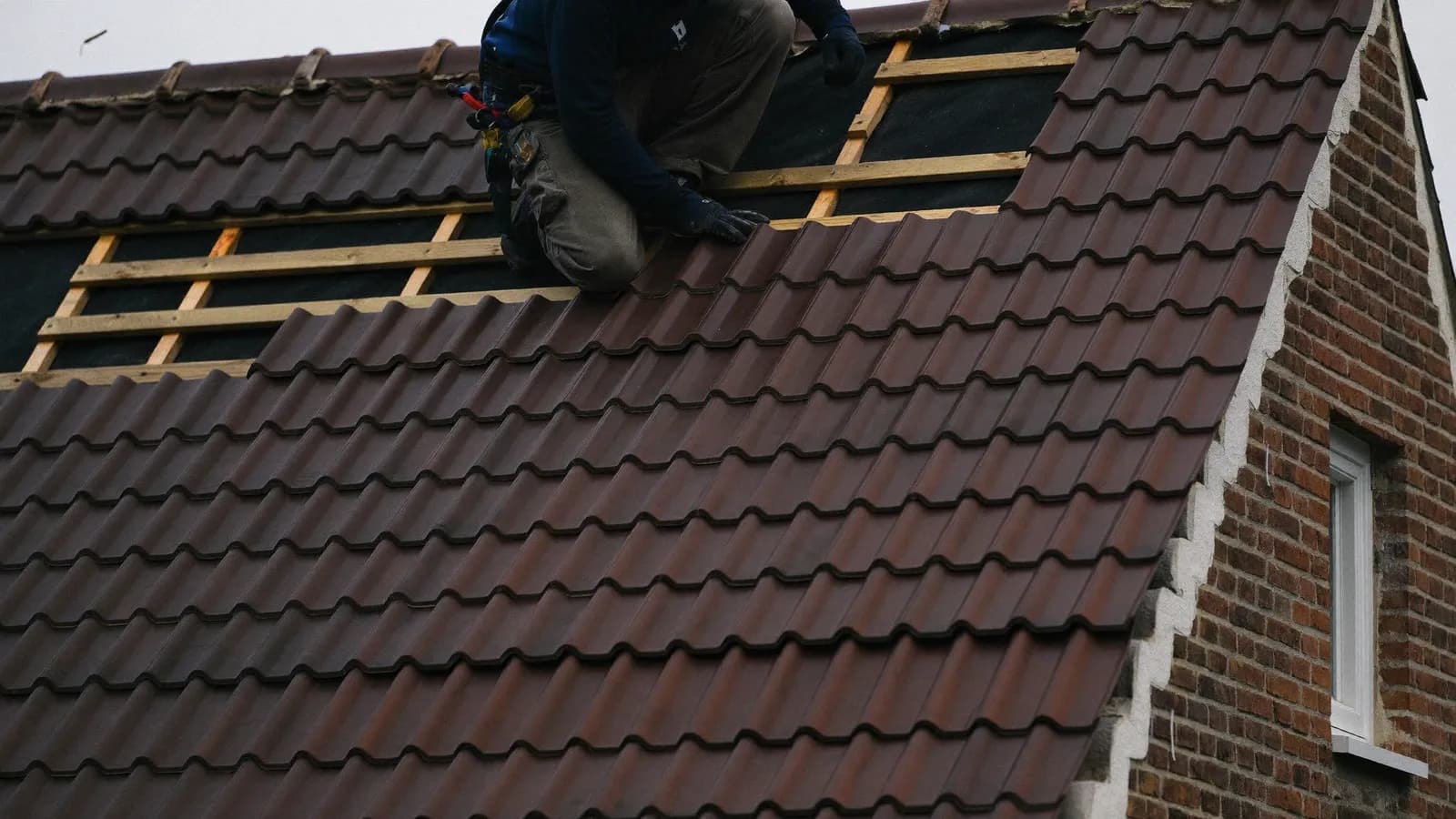Dakwerker legt keramische pannen op een hellend dak, met panlatten en onderdak zichtbaar op het onafgewerkte deel