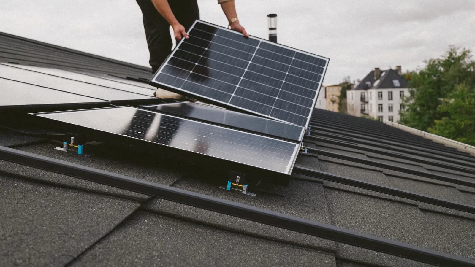 Installateur schuift een zonnepaneel op de montagerails van een pannendak, naast een rij geplaatste panelen